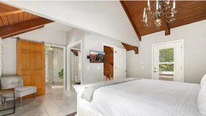 Un dormitorio con una cama grande, vigas de madera en el techo, un banco y una puerta que da a otra habitación.