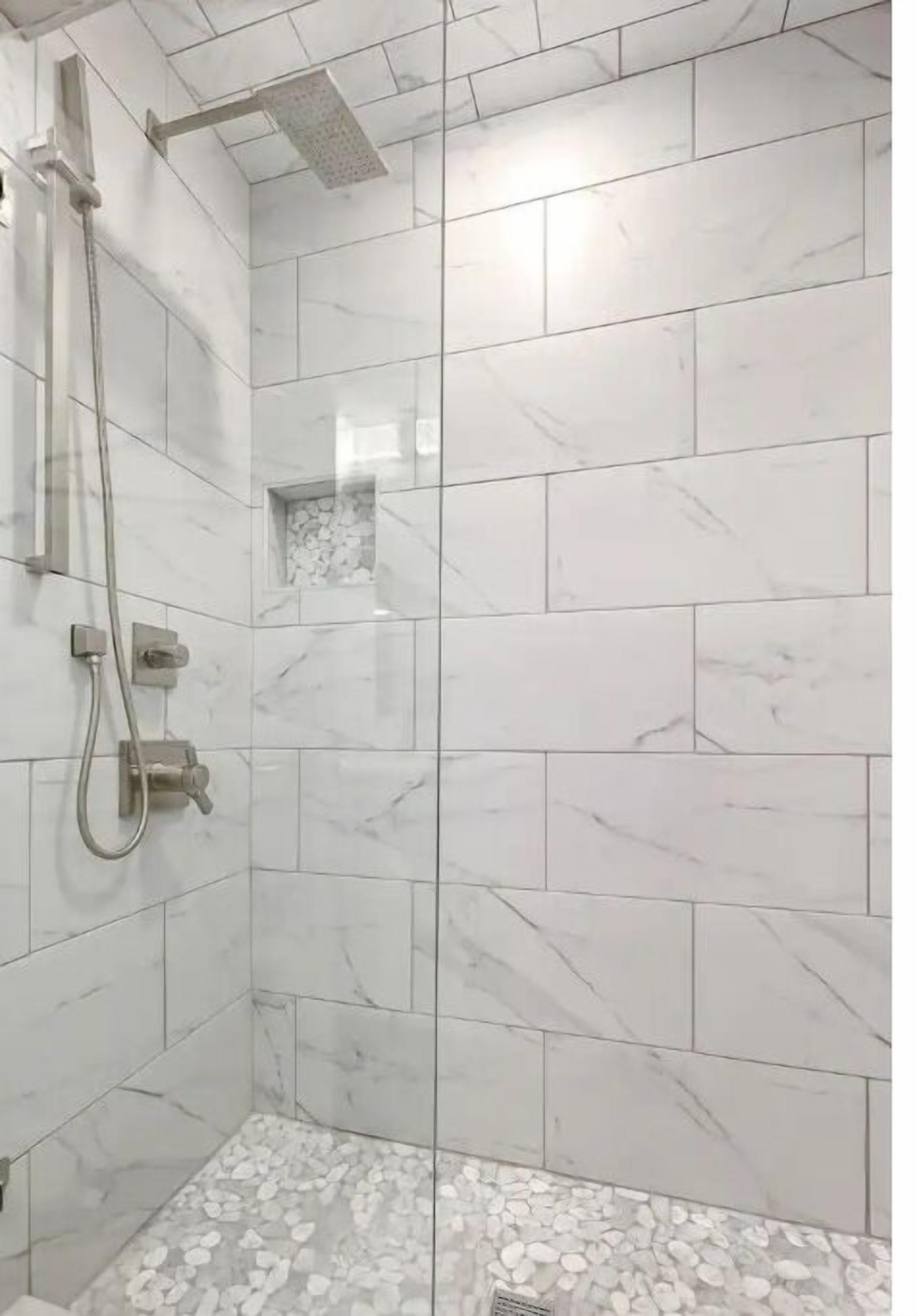 A shower area with white marble tiles and a showerhead.