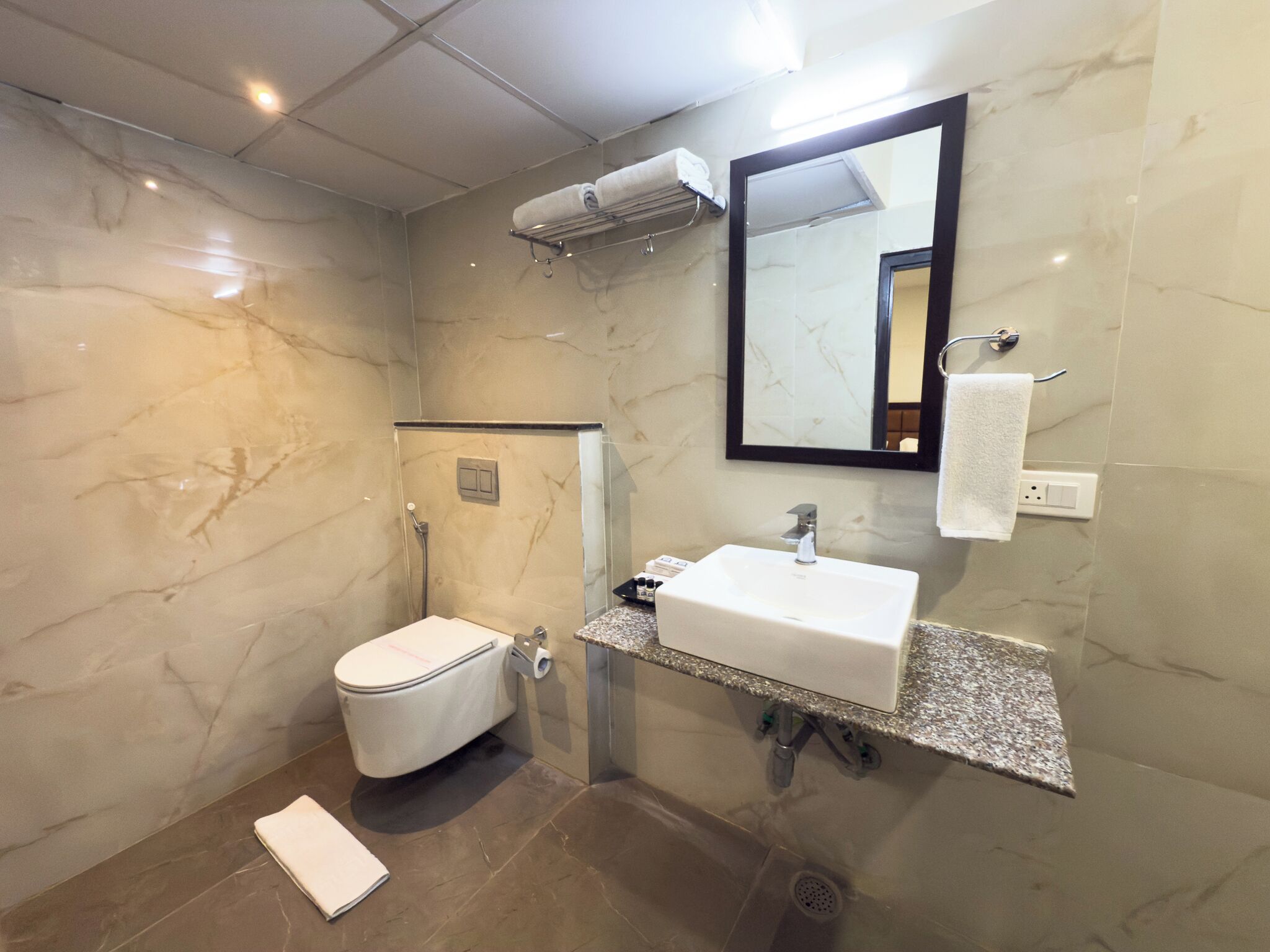 Une salle de bain moderne avec un mur en marbre, des toilettes blanches, un lavabo avec un miroir et un porte-serviettes.
