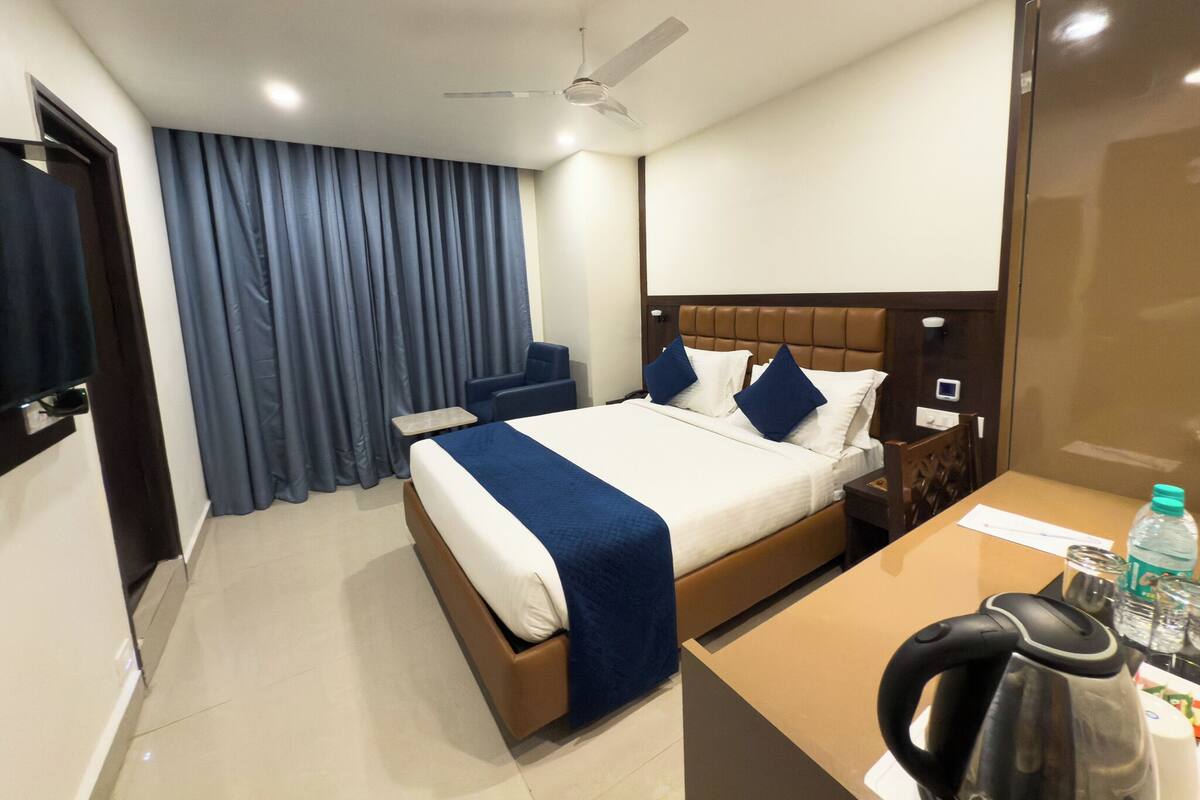 Una habitación de hotel con cama, escritorio, silla, cafetera y cortina.