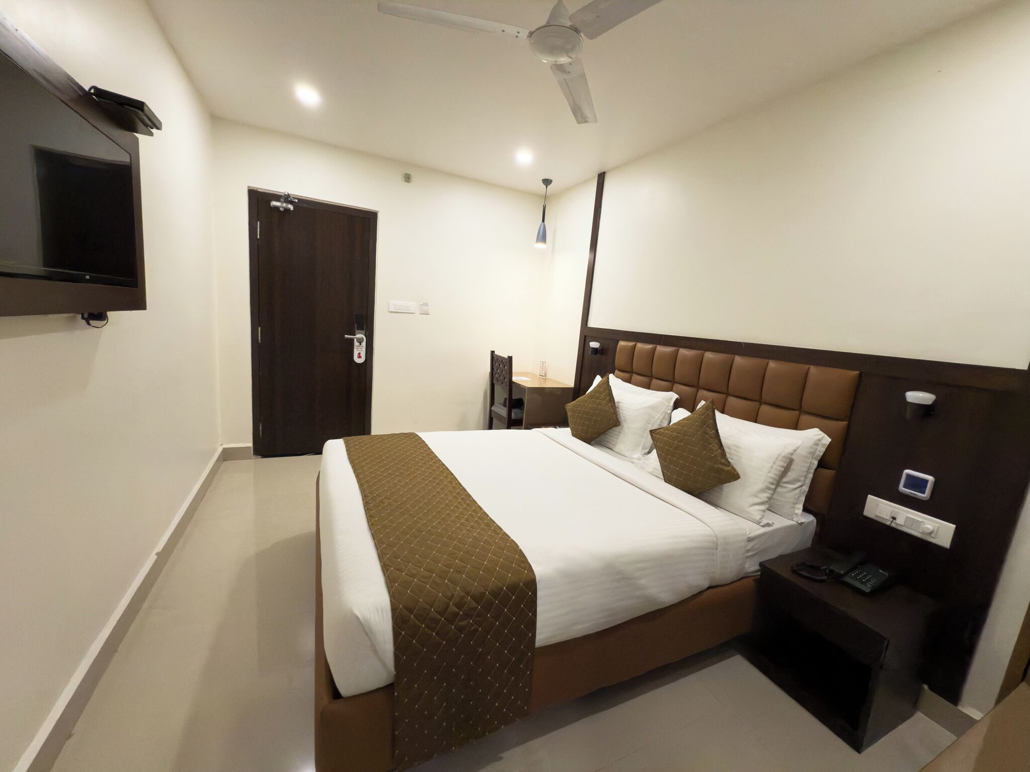 Habitación de hotel con cama, mesita de noche, televisor y ventilador de techo.