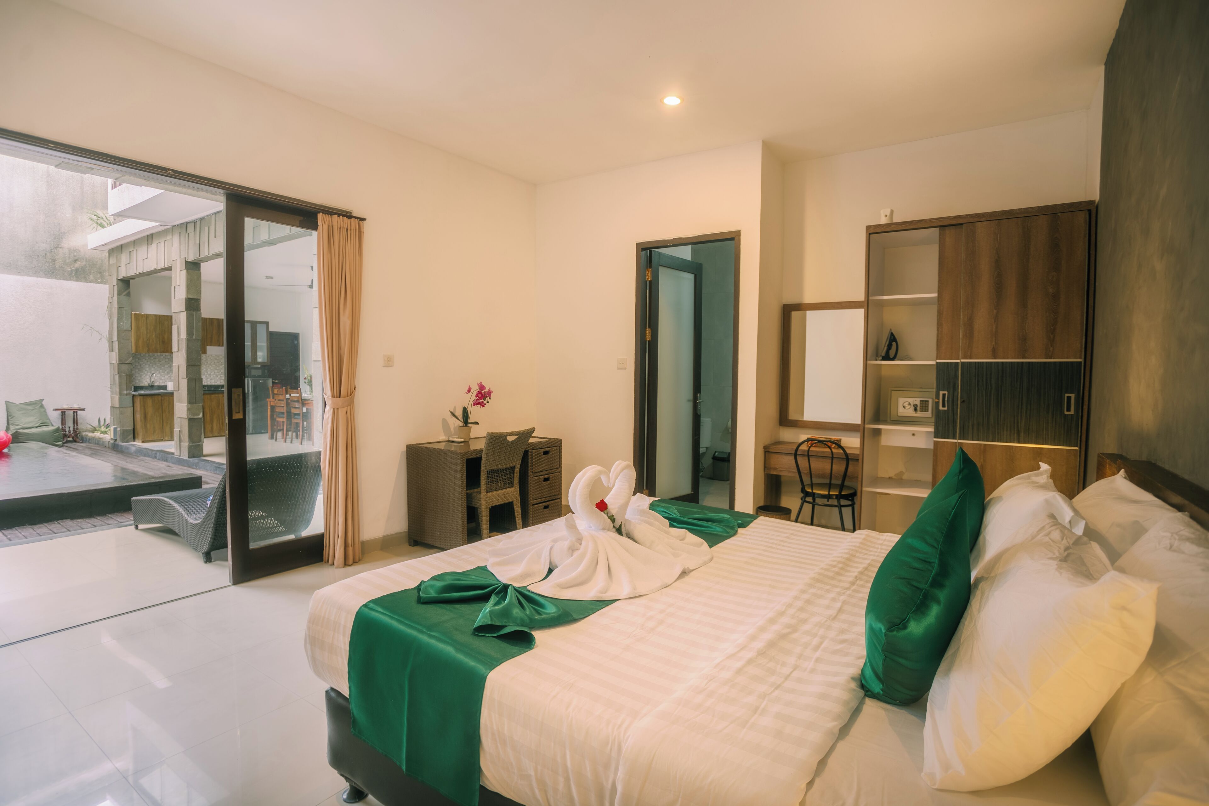 A hotel room with a bed, a desk, a chair, a wardrobe, and a sliding glass door leading to an outdoor area.