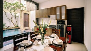 A dining area with a table set for six, a kitchen in the background, and a pool visible through the open door. - Taman Bali Villa Kerobokan (Kerobokan)