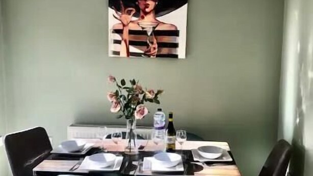A dining area with a table set for four, a vase with flowers, and a painting on the wall. - 3 Bed House - Sleeps 6 - Garden - Parking (Bristol)