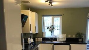 A compact kitchen with white cabinets, a black countertop, and a window with a view of buildings. - 3 Bed House - Sleeps 6 - Garden - Parking (Bristol)