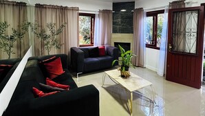 A modern living room with a black sofa, a coffee table, and a potted plant. There are curtains on the windows and a door with a metal gate. - Pousada do Lago Gramado (Gramado)