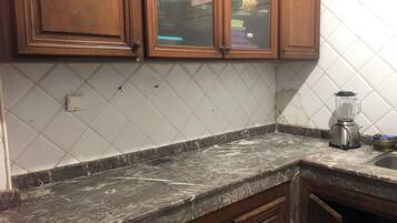 A kitchen with wooden cabinets, a marble countertop, and a blender on the counter.