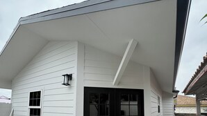 Un bâtiment blanc avec une porte et des fenêtres noires, un toit en pente et un plancher en béton.