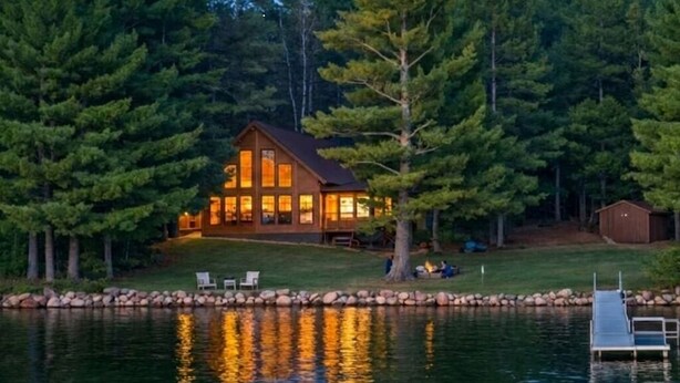 A cabin with a dock, surrounded by trees, and a small shed nearby.