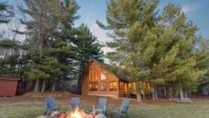 A cabin with a fire pit and chairs in the yard.