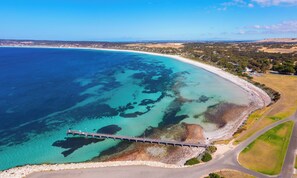 An aerial view of a coastal area with a pier extending into the turquoise waters, surrounded by a mix of sandy beaches and grassy fields.