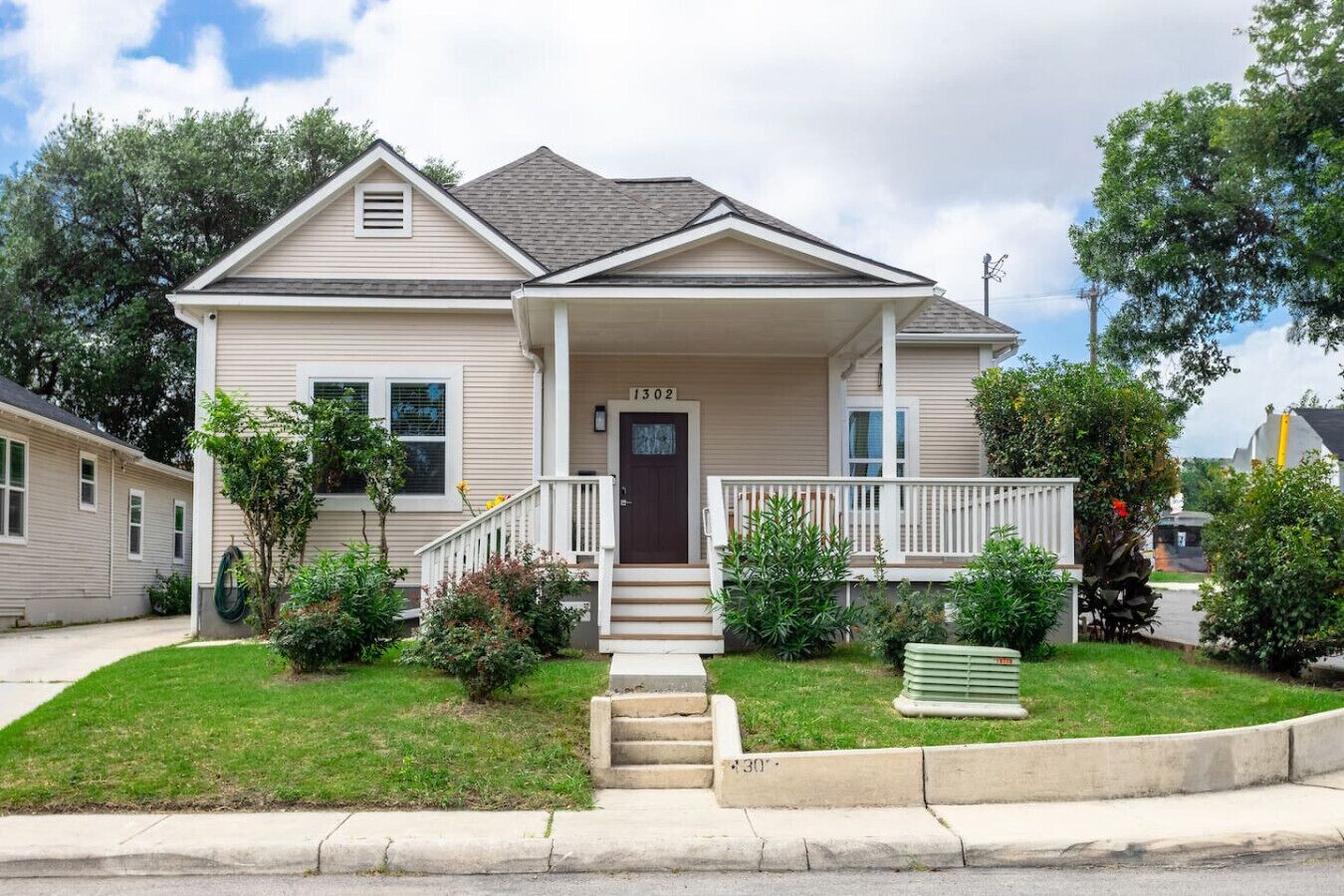 A two-story house with a front porch, a front door, and a small front yard with a lawn and a few shrubs.