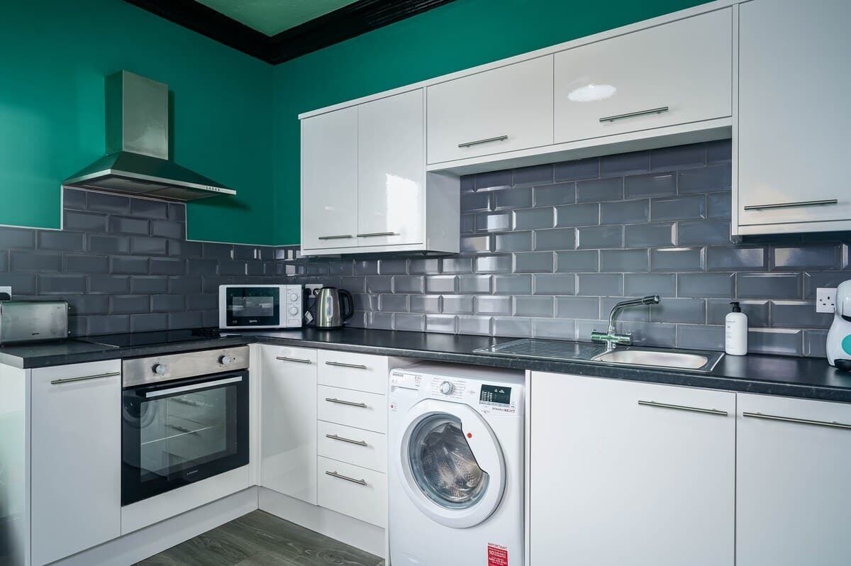 A compact kitchen with white cabinets, a built-in microwave, a toaster, a washing machine, and a sink.