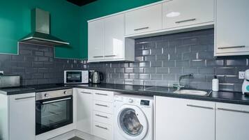 A compact kitchen with white cabinets, a built-in microwave, a toaster, a washing machine, and a sink.