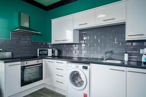 A compact kitchen with white cabinets, a built-in microwave, a toaster, a washing machine, and a sink.