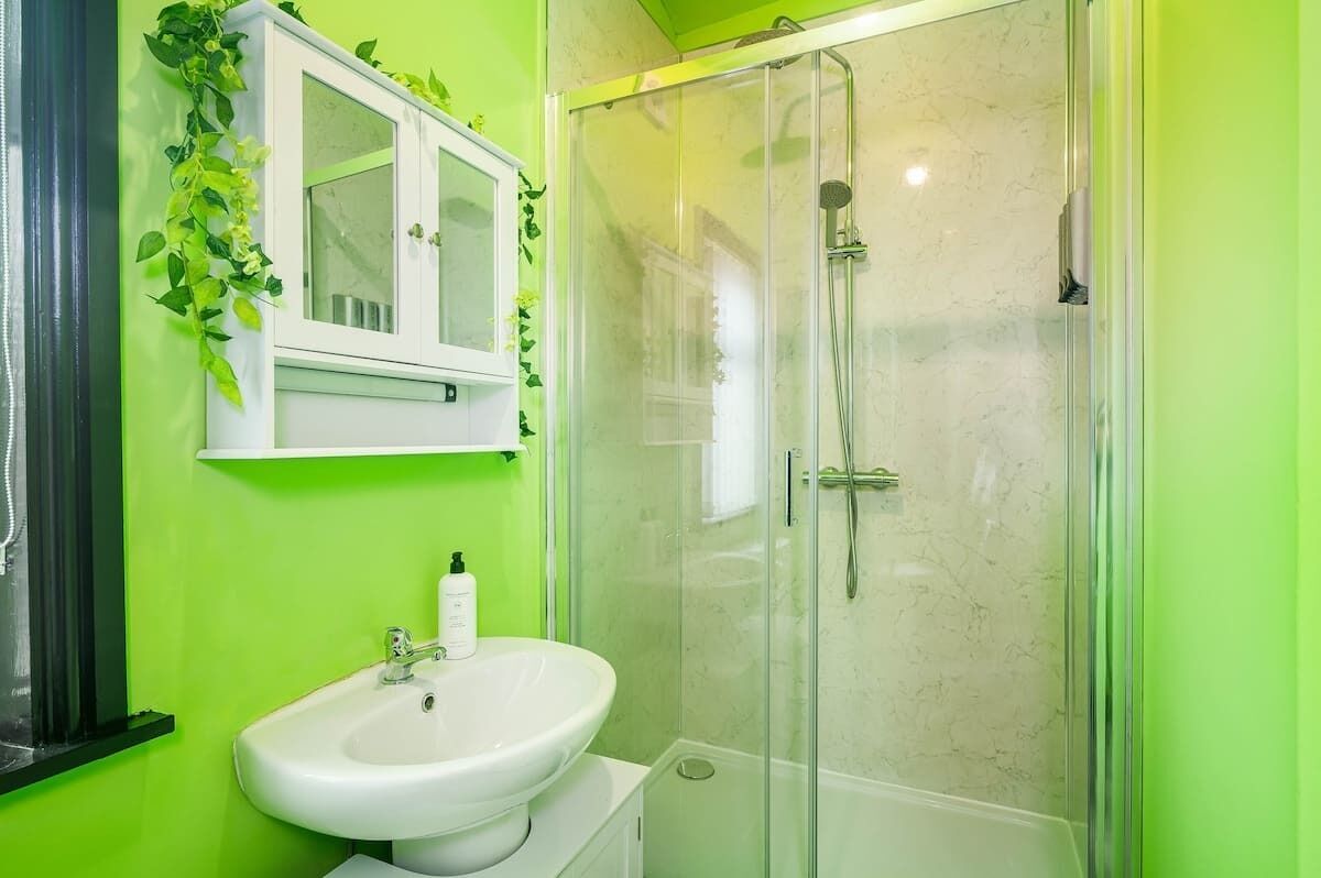 A bathroom with a white sink, a glass-enclosed shower, and a green wall.