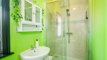 A bathroom with a white sink, a glass-enclosed shower, and a green wall.