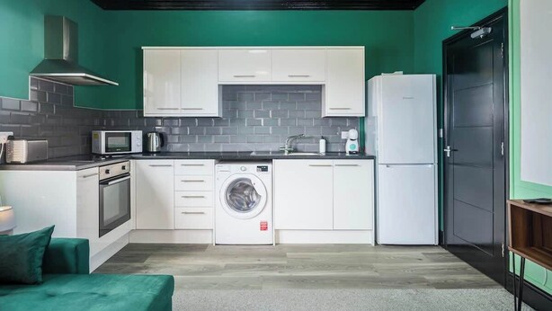 Una cocina compacta con armarios blancos, microondas integrado, lavadora y refrigerador.