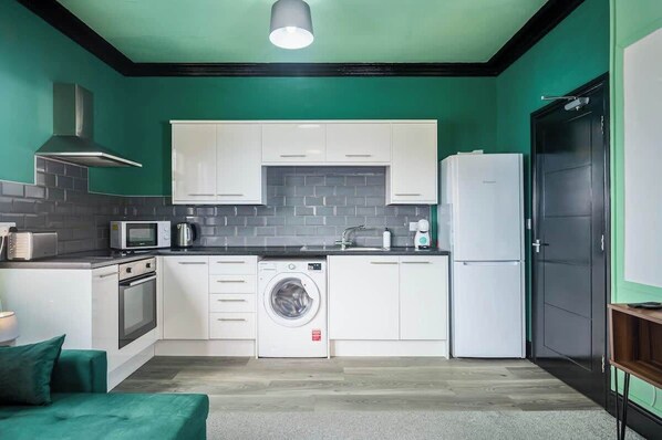 Una cocina compacta con armarios blancos, microondas integrado, lavadora y refrigerador.