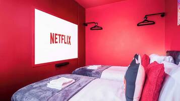 Een kamer met twee bedden, rode wanden, een groot raam met het Netflix logo, en twee zwarte kledinghangers aan de muur.