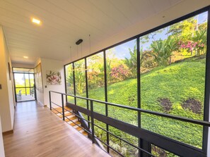 A modern interior with a wooden staircase leading to a balcony overlooking a lush garden.