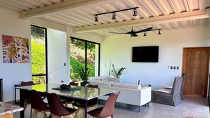 A modern kitchen with a dining area, large windows, and a TV mounted on the wall.