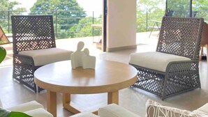A modern living room with wicker furniture, a round wooden table, and a large sliding glass door leading to an outdoor area.