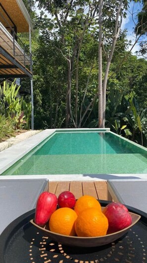 Ein Pool mit Blick auf Bäume und eine Schale Obst auf der Terrasse.