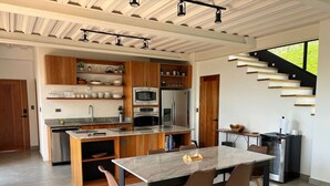 A modern kitchen with wooden cabinets, stainless steel appliances, and a dining area with a marble table and brown chairs.