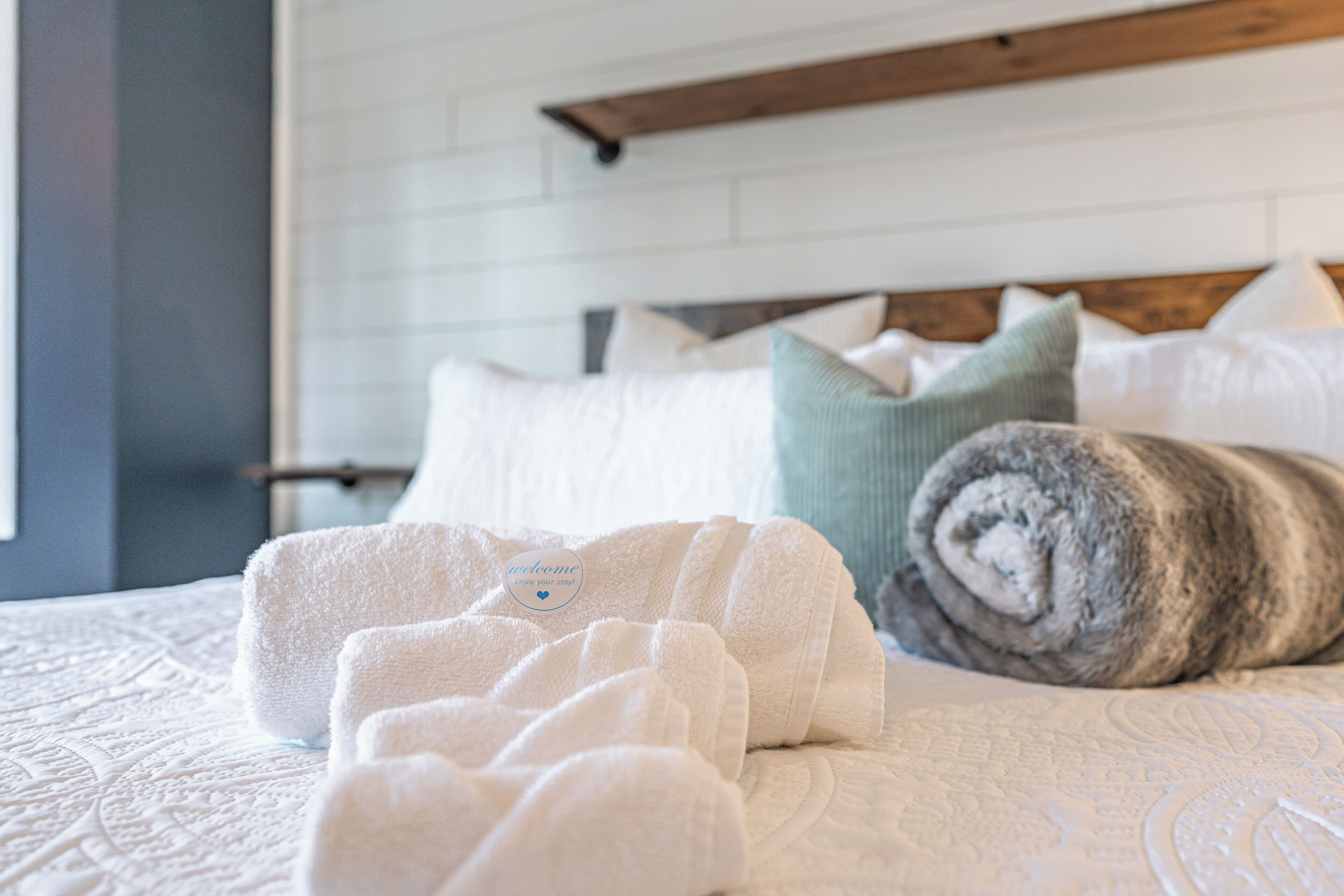 Een netjes opgemaakt bed met witte en grijze handdoeken, een houten hoofdbord en een witte bakstenen muur.