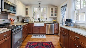 A kitchen with wooden cabinets, stainless steel appliances, a granite countertop, and a red patterned rug. - Endearing Lakeside Private Retreat  (Hendersonville)