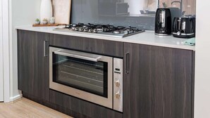 A modern kitchen with dark wood cabinets, a stainless steel range hood, a built-in oven, and a countertop with a toaster and kettle.