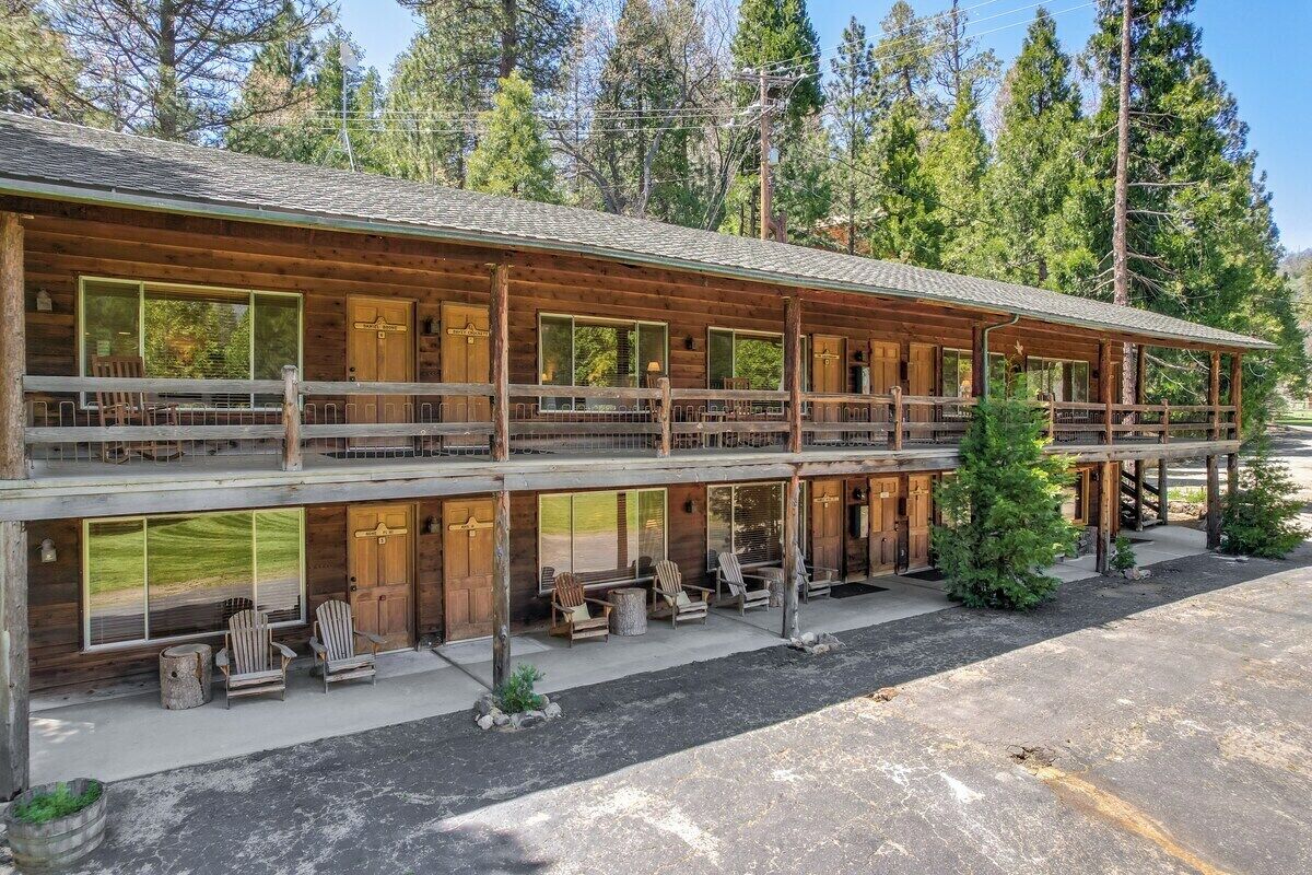 A two-story log cabin with a balcony, large windows, and outdoor seating.