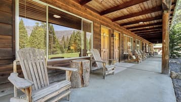 A covered outdoor seating area with wooden chairs and tables, large windows with a mountain view, and a wooden building structure.