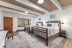 A bedroom with two wooden beds, a desk, and a window with a view of greenery.