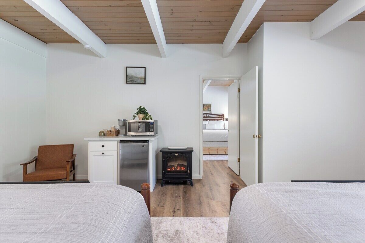 Un dormitorio con dos camas, techo de madera, una kitchenette pequeña y una chimenea.