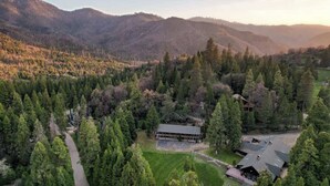 A lodge surrounded by dense forest and mountains, with a clear path leading to the entrance. - Camp Nelson Lodge | Room 4 | Sierra Nevada Retreat (Springville)