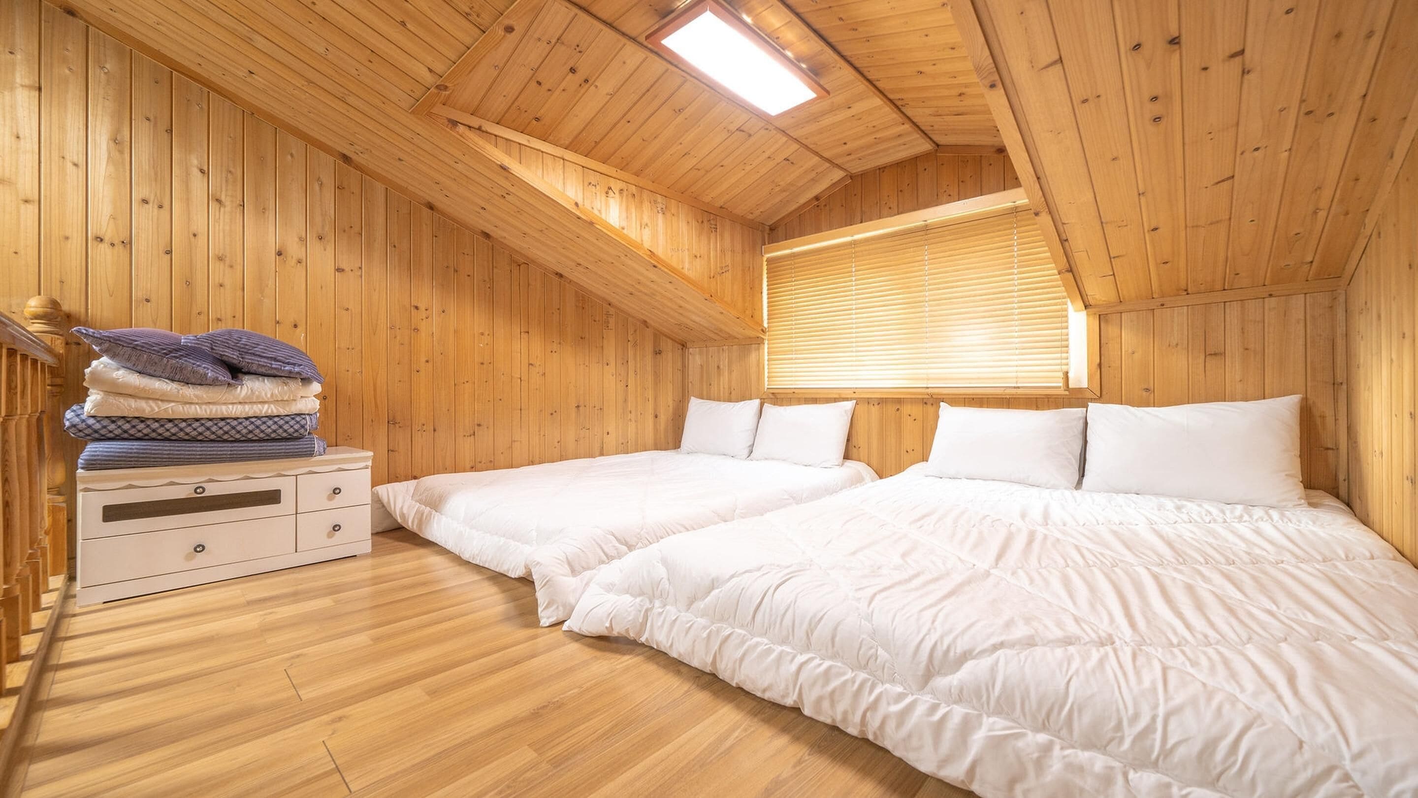 A wooden cabin bedroom with two beds, a nightstand, and a window with blinds.