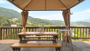 A wooden deck with a picnic table and a grill, overlooking a mountainous landscape. - Gapyeong Gold Castle Pension (Gapyeong)