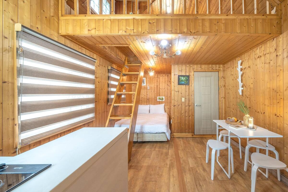 Ein gemütliches Blockhaus-Interieur mit Schlafkoje, Essbereich mit Tisch und Stühlen sowie Holzboden und sichtbaren Balken.