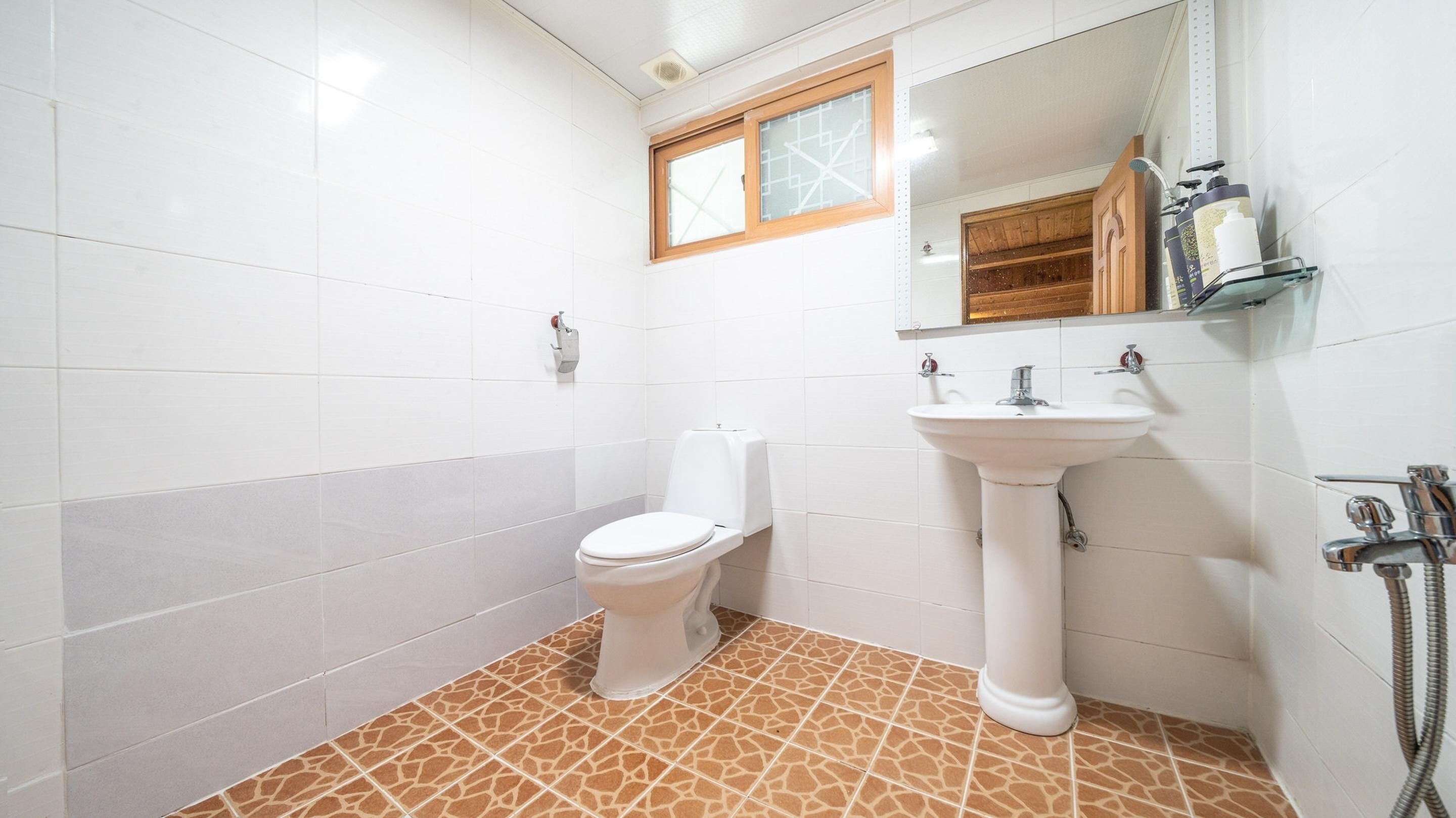 Et badeværelse med hvide fliser, et hvidt toilet, en konsolvask og en brusekabine.