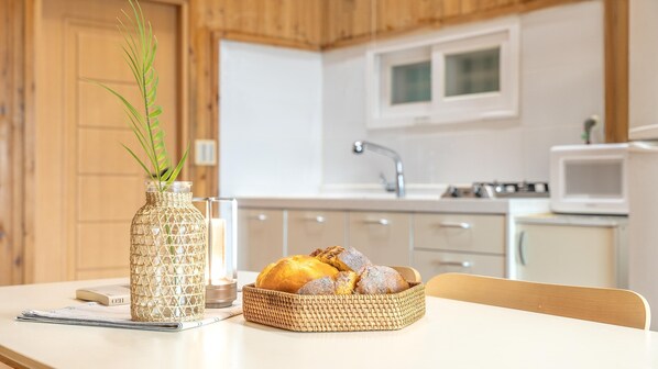 Een keuken met witte kastjes, een magnetron en een rieten mand met brood op een tafel.