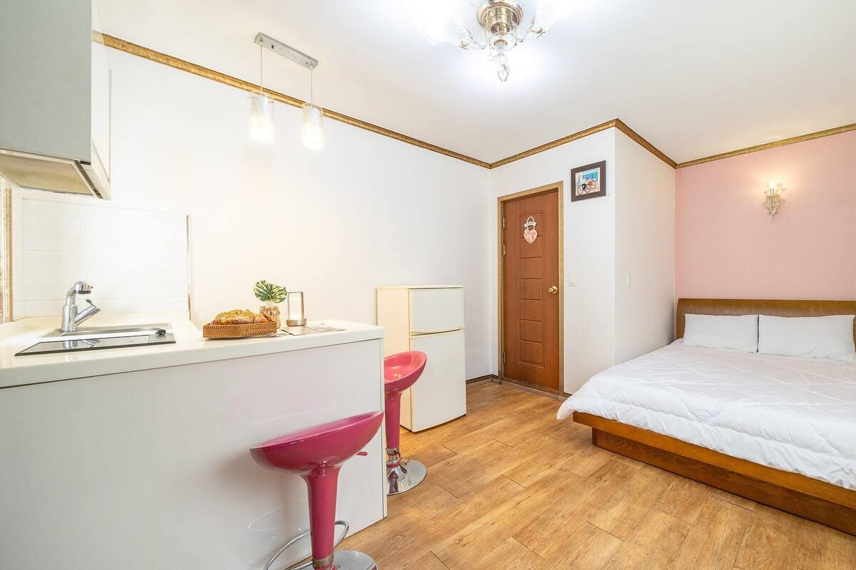 Ein Schlafzimmer mit einem hölzernen Bett, einem weißen Nachttisch, einem rosa Waschbecken und einer Tür mit Herzverzierungen.