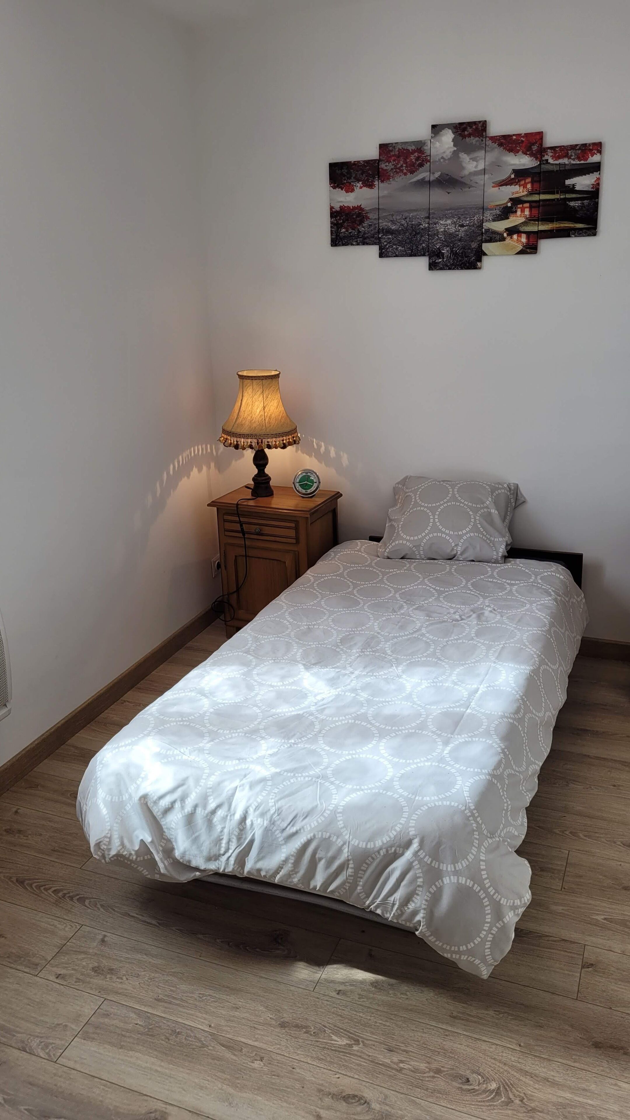 Ein Schlafzimmer mit einem Bett, einem Nachttisch mit Lampe, einer Wanduhr und mehreren gerahmten Bildern.
