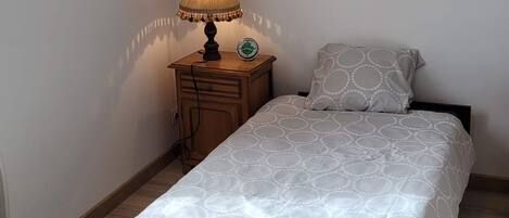 Un dormitorio con una cama, una mesita de noche con una lámpara, un reloj de pared y varias fotografías enmarcadas.