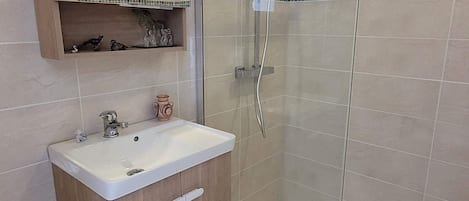 Un baño moderno con ducha envuelta en vidrio, tocador de madera con lavamanos y un espejo sobre el tocador.