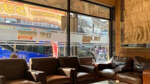 Un hall d’hôtel avec des canapés en cuir, une grande fenêtre donnant sur la rue et un mur orné de sculptures d’éléphants.