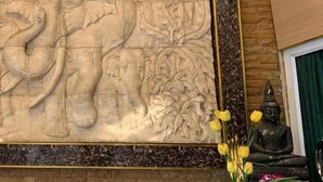 Une pièce ornée d’une grande sculpture d’éléphant sculptée sur le mur, d’une statue de Bouddha et d’un vase rempli de fleurs jaunes.