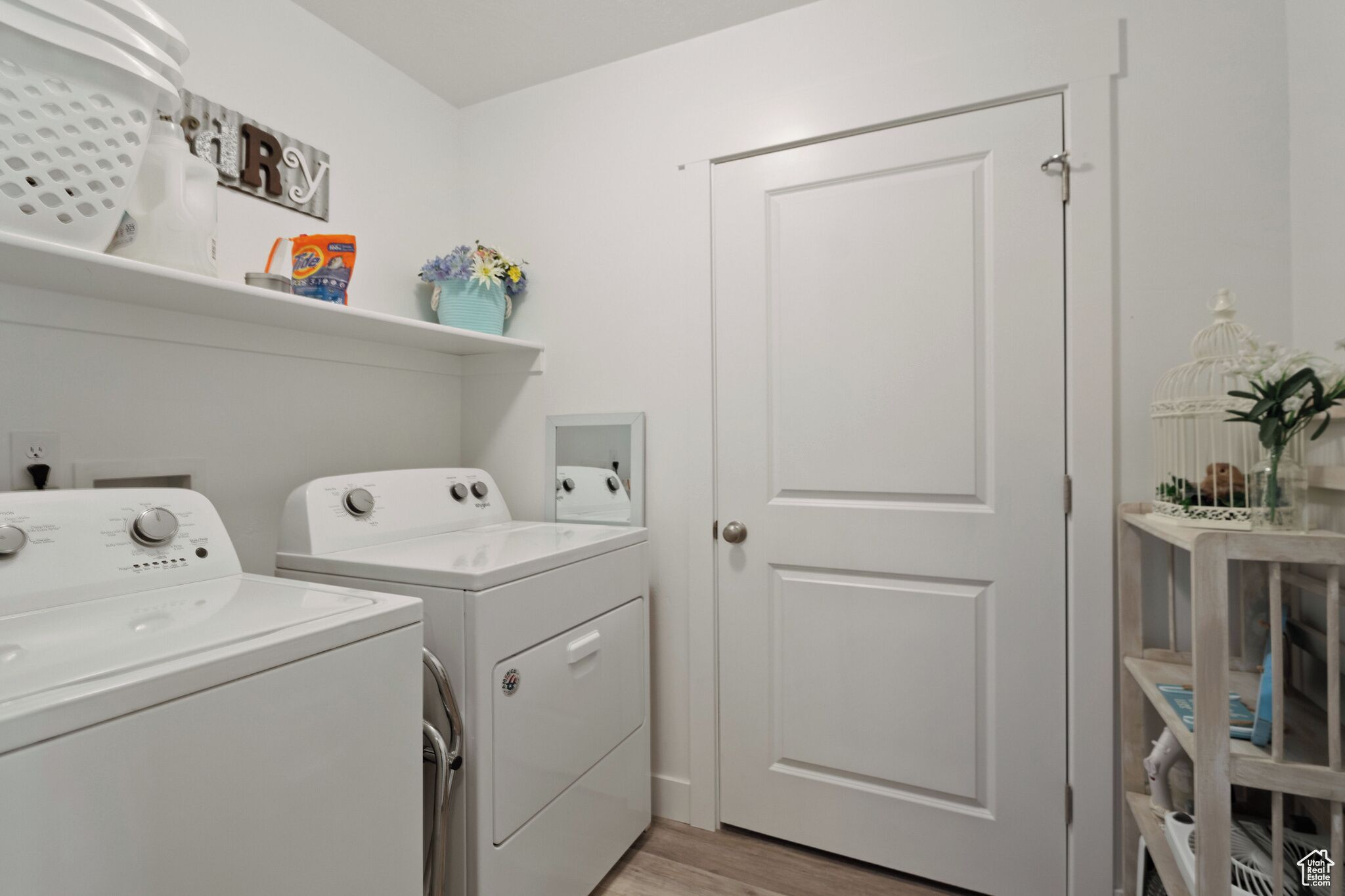 A laundry room with two white washing machines, a dryer, and a shelf with laundry supplies.