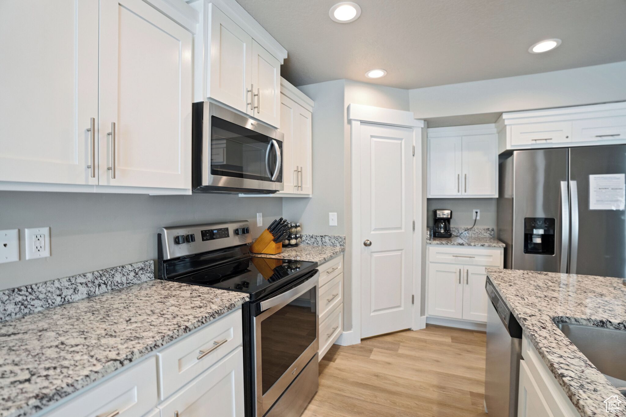 A modern kitchen with white cabinets, granite countertops, stainless steel appliances, and a wooden floor.